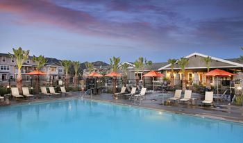 a swimming pool with chairs and umbrellas at dusk